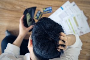 Asian man holding wallet with money and thinking about finding money to pay credit card debt