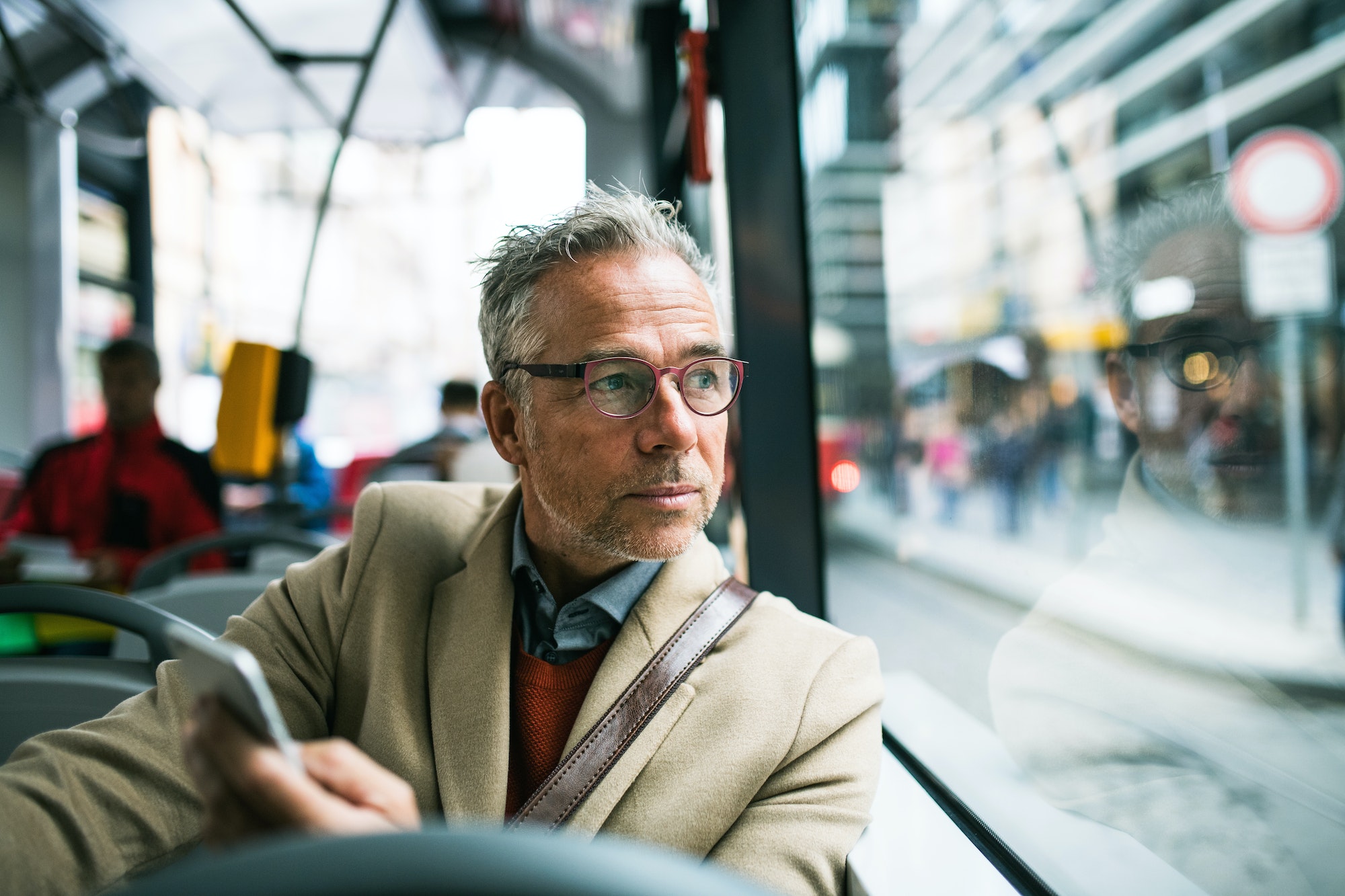 Mature businessman with smartphone travelling by bus in city.