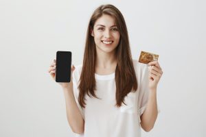 Money in your phone. Portrait of attractive young woman holding smartphone and credit card, happy
