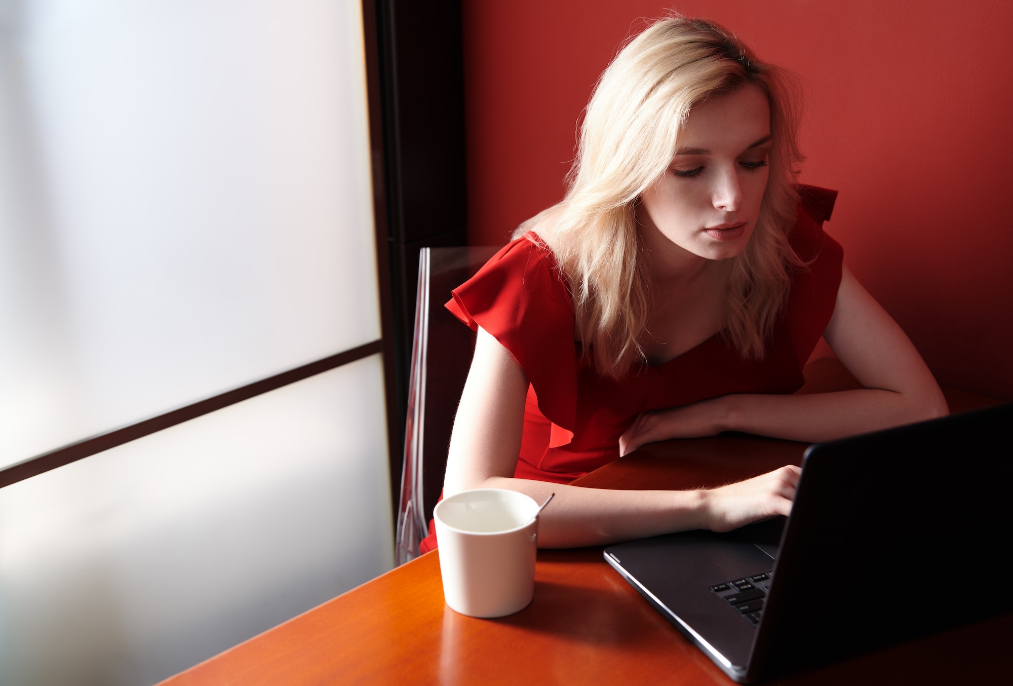 Young adult woman wearing red jumpsuit and using laptop