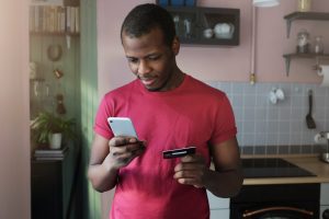 Young African American man holds smartphone in one hand and credit card in another